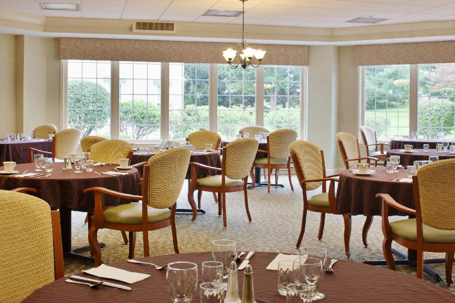 An elegant dining room with neatly set tables and comfortable chairs, featuring large windows that allow natural light to fill the space.