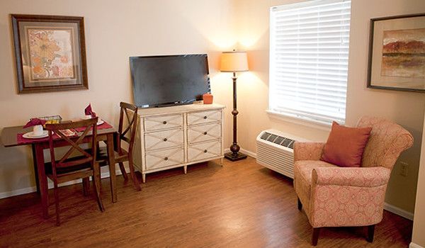 A cozy living room with a TV on a dresser, a lamp, and an armchair.