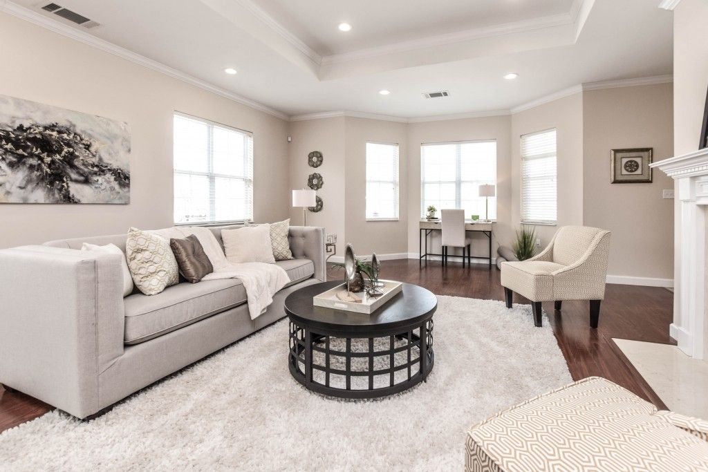 A bright and cozy living room with a neutral color scheme, featuring a comfortable sofa, round coffee table, armchair, and large windows that let in plenty of natural light.