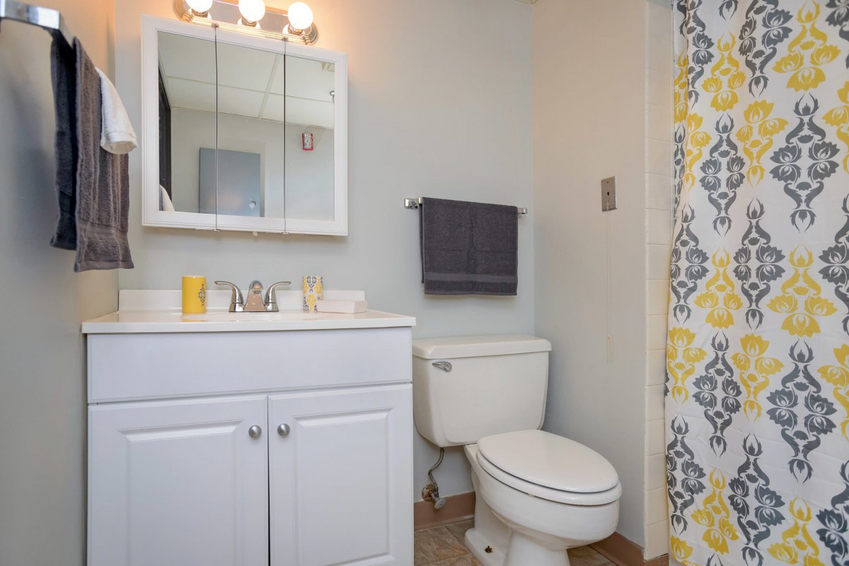 A small bathroom with a sink, mirror, toilet, and a colorful shower curtain.