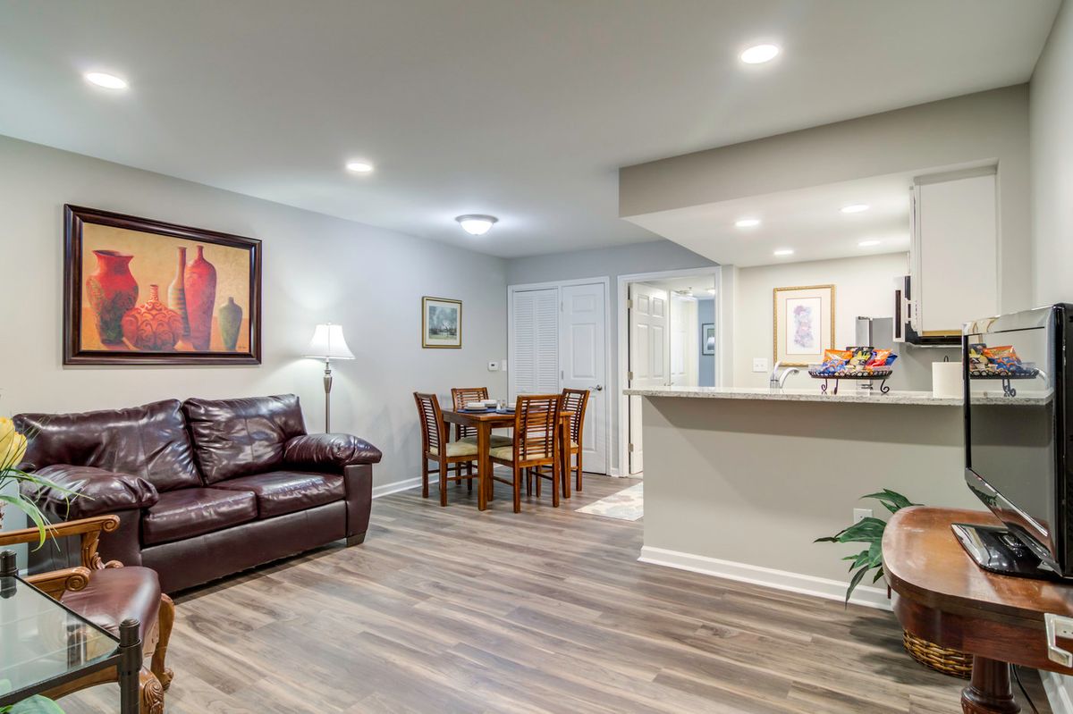 A modern living room with a cozy seating area and adjacent dining table, featuring stylish decor and wooden flooring.