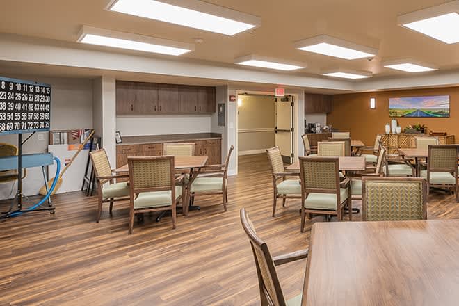 A spacious dining area with wooden flooring and neatly arranged tables and chairs.