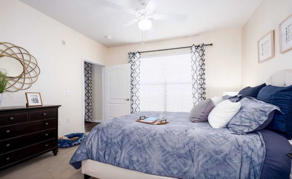 A cozy bedroom with a neatly made bed, patterned curtains, and a ceiling fan.