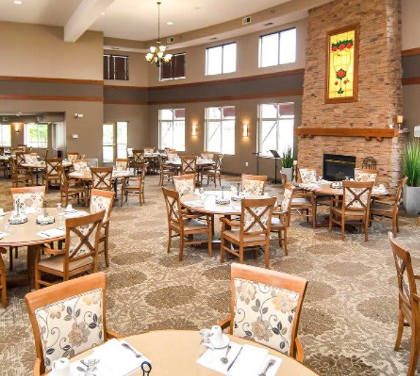 A spacious and elegantly furnished dining area featuring round tables, cushioned chairs, and a cozy fireplace.