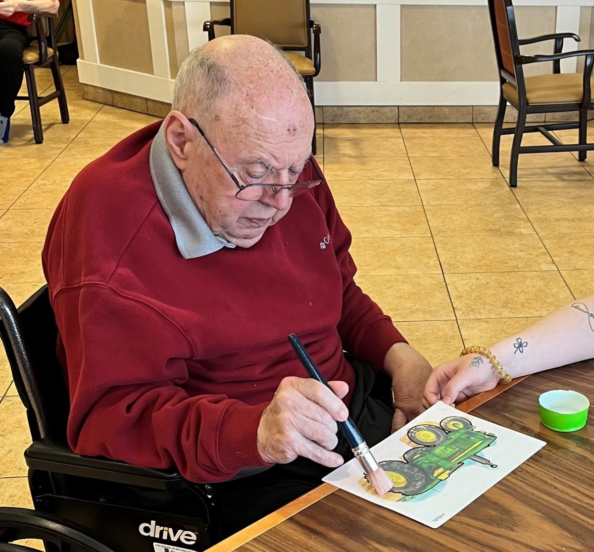 An elderly man is engaged in painting at a table, participating in an art activity.