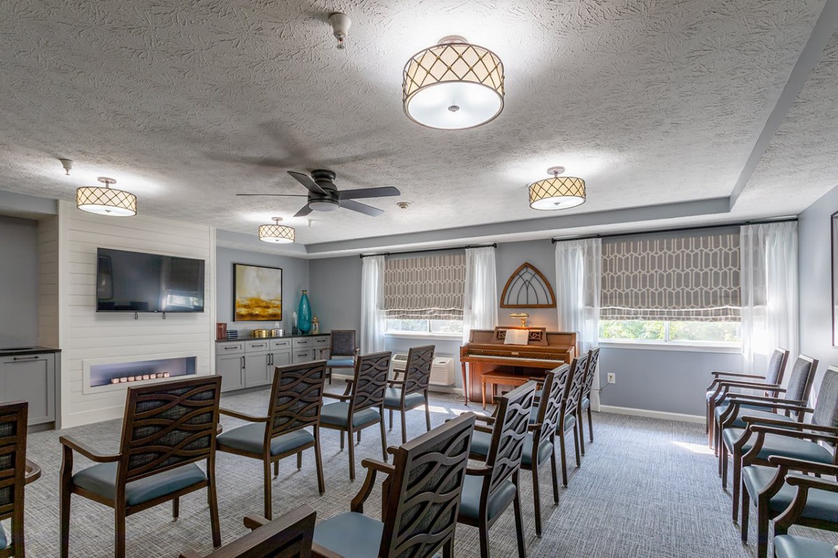 A well-lit meeting room with arranged chairs, a piano, and modern ceiling lights.