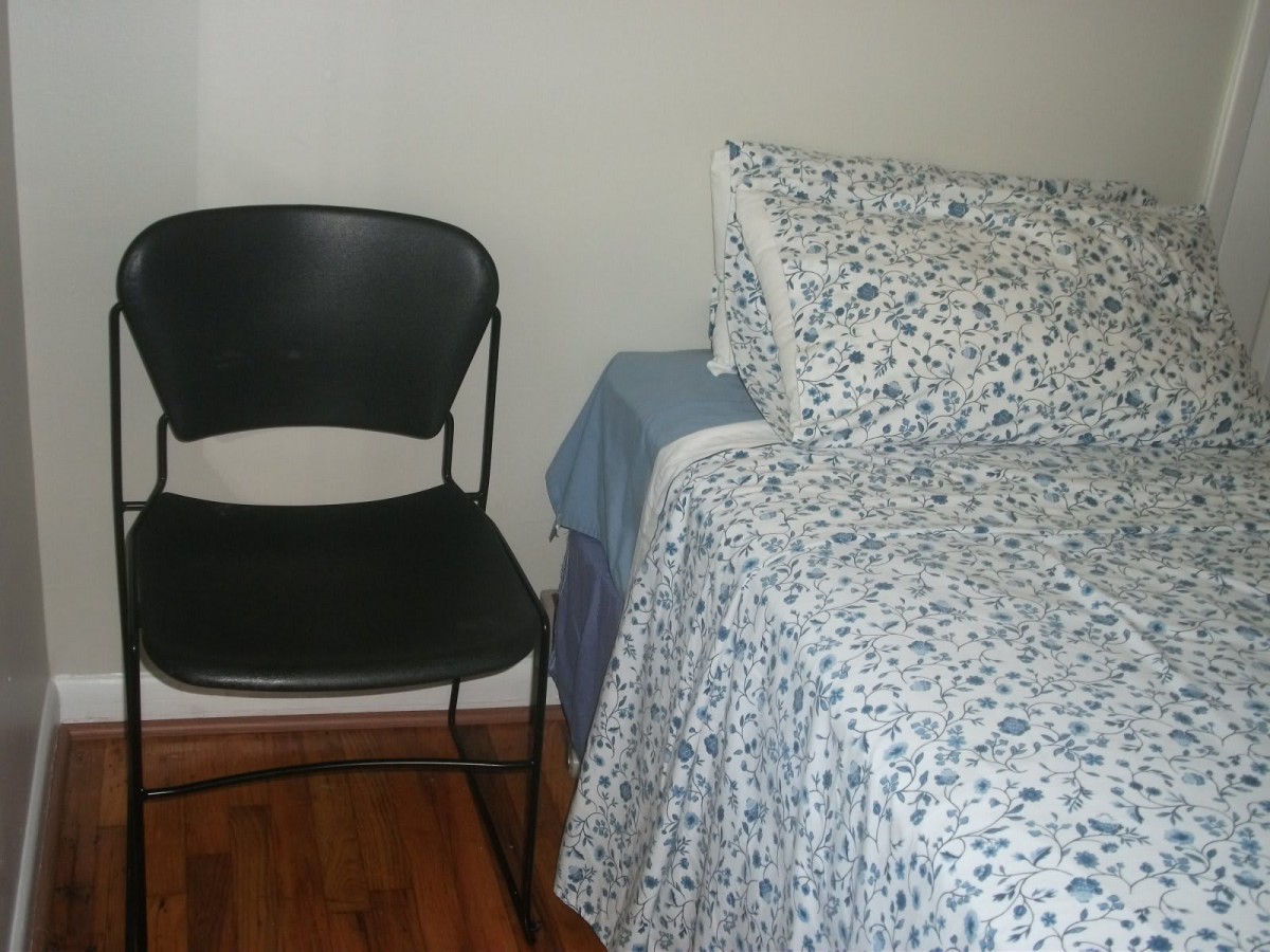 A simple bedroom setup with a chair next to a bed covered in patterned bedding.