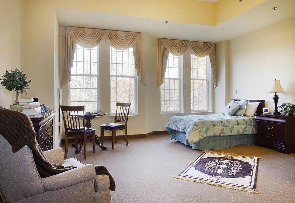 A cozy bedroom with large windows, a bed, and elegant curtains letting in natural light.