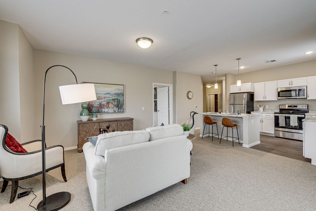 A modern open floor plan features a cozy living room with a white sofa, adjacent to a kitchen area with bar stools and pendant lighting.