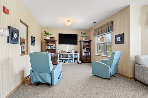 A cozy living room featuring two comfortable blue chairs and a television, complemented by bookshelves and decorative plants.