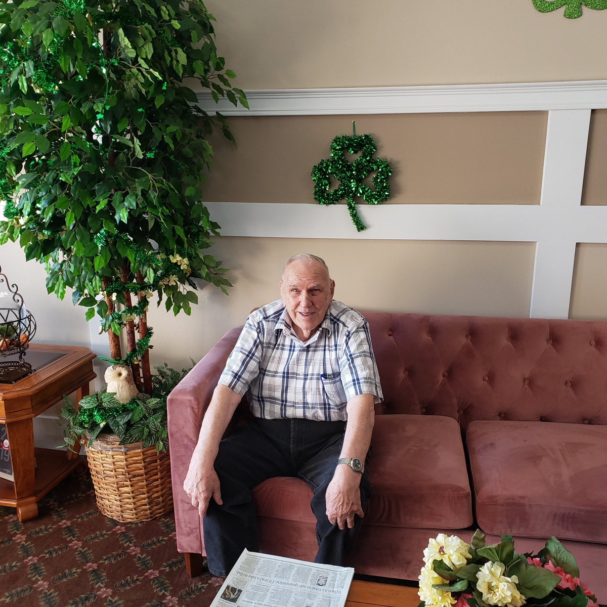 A man sitting on a sofa in a living room with plants around.
