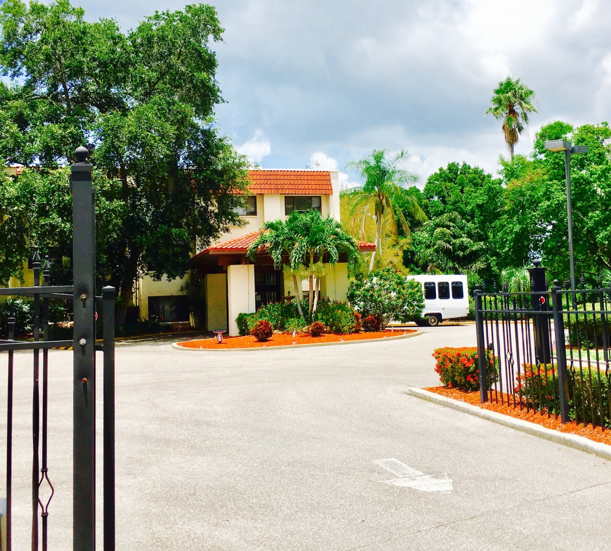 Entrance to a building surrounded by lush greenery and a fenced driveway.