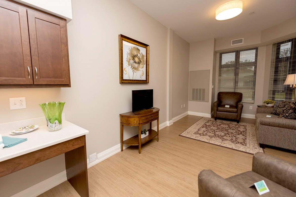 A minimalist living room with neutral tones, featuring a small television, armchair, and decorative artwork.