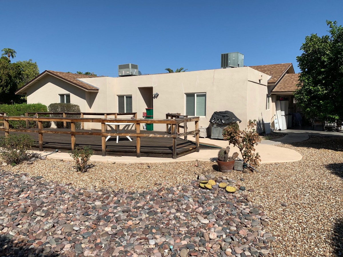 A house with a deck and gravel landscaping in the yard under a clear blue sky.