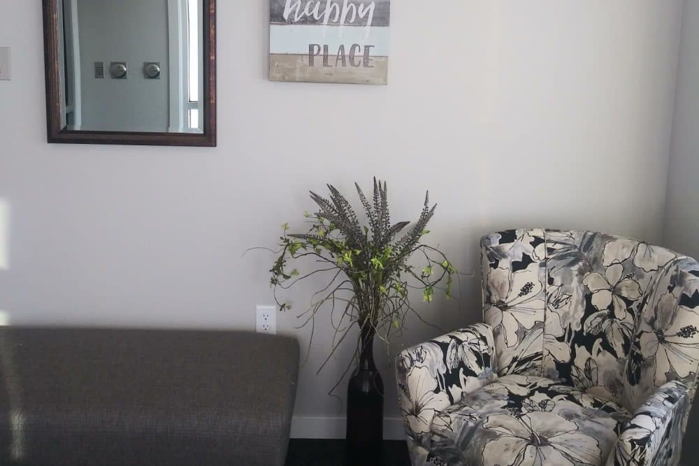 A cozy corner of a living room with a floral armchair, decorative plant, and wall art bringing a sense of peace.