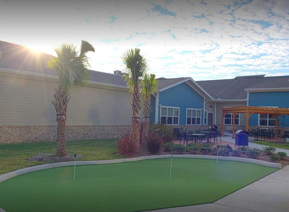 A sunny view of a building with palm trees and a putting green in the foreground.