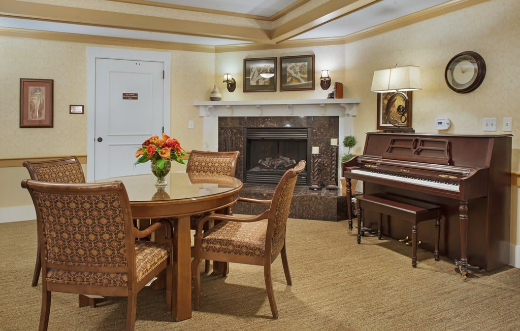 A cozy living room featuring a piano, fireplace, and a round table with chairs.
