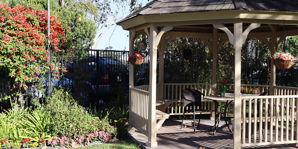 A charming gazebo in a sunlit garden with a wooden bench and hanging flower basket.
