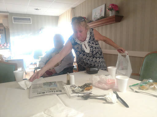 A woman in a patterned dress organizing items on a table, with another person seated nearby.