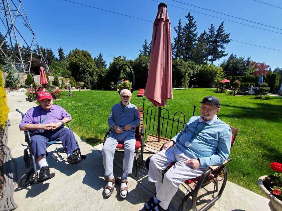 A group of elderly people sitting outdoors in a garden on a sunny day.