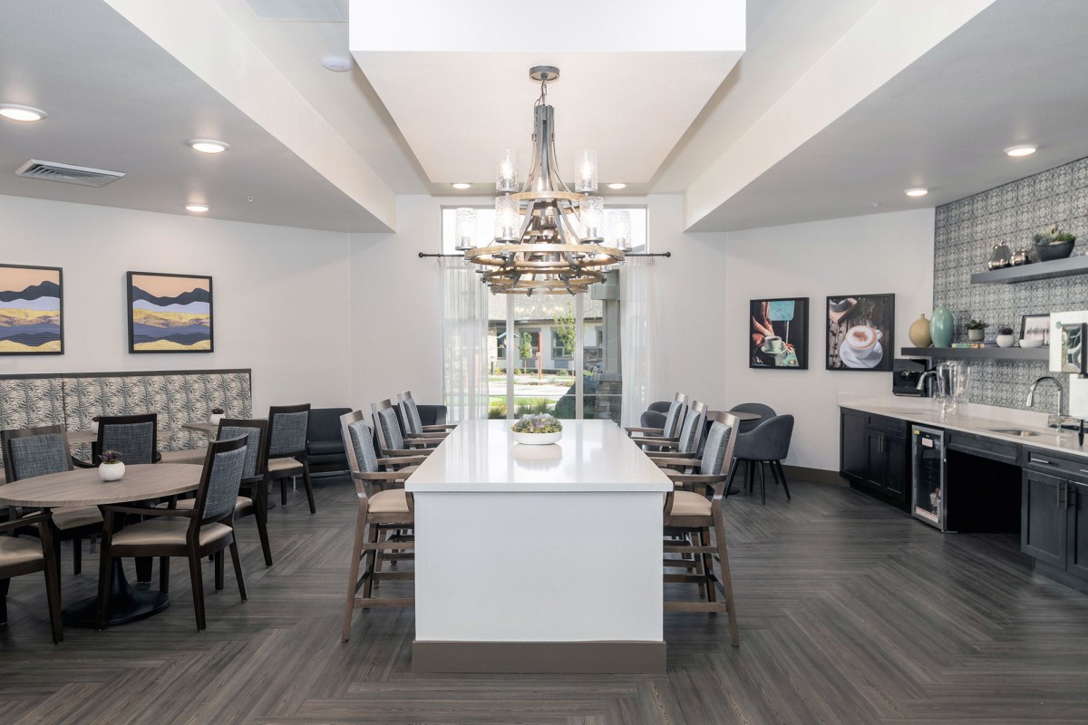 A modern dining room featuring a long table with chairs and a central chandelier.