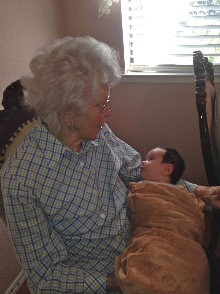 An elderly person lovingly holding a baby indoors, showcasing a moment of family bonding.