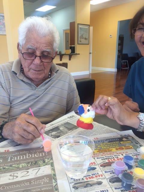 An elderly man participating in a craft activity, painting a small figurine with colorful paints.