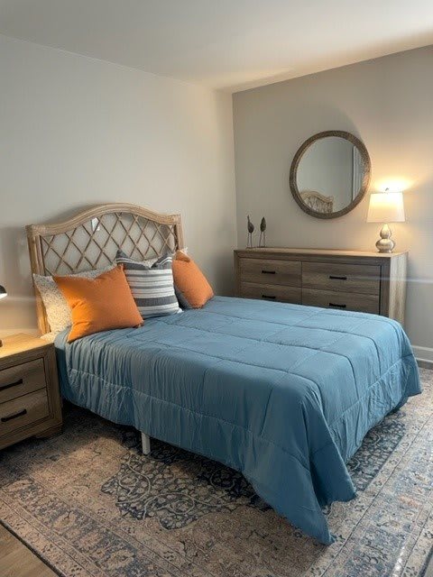 A cozy bedroom with a blue bedspread, orange and striped pillows, and modern wooden furniture.