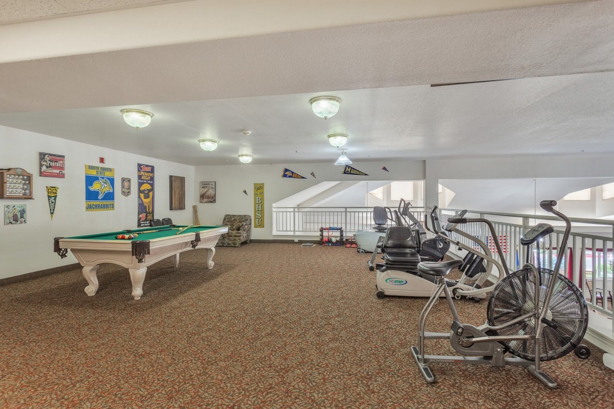 A spacious room featuring fitness equipment and a pool table, combining leisure and exercise facilities.
