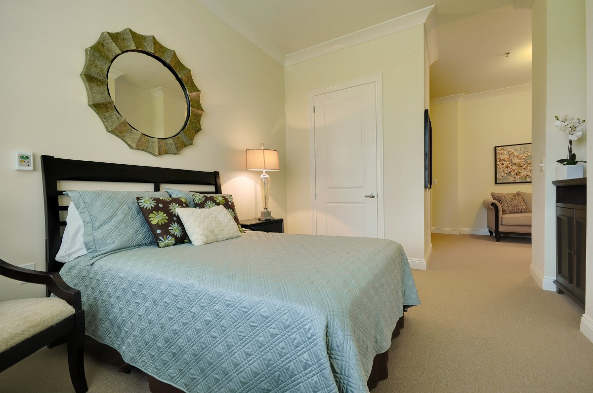 A cozy bedroom with a neatly made bed, decorative mirror, and ambient lighting.