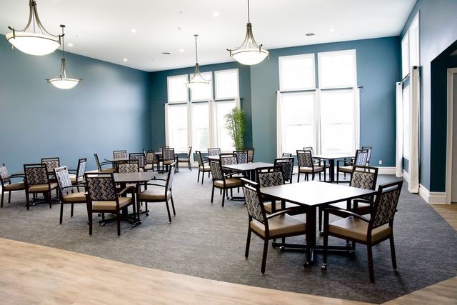 A modern dining area with multiple tables and chairs, illuminated by large windows and stylish ceiling lights.