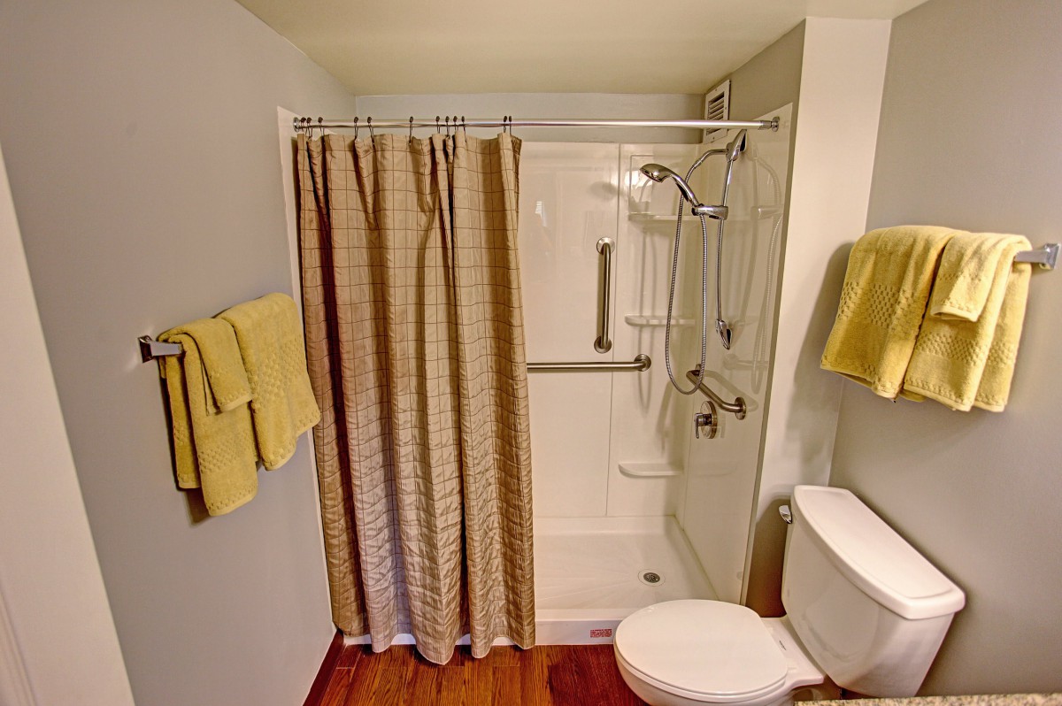 A bathroom with a shower area equipped with handrails, a curtain, and a toilet with yellow towels.