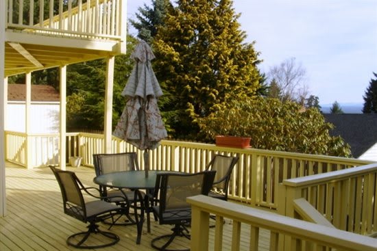 A sunny deck featuring a patio table with chairs and an umbrella, surrounded by lush trees.