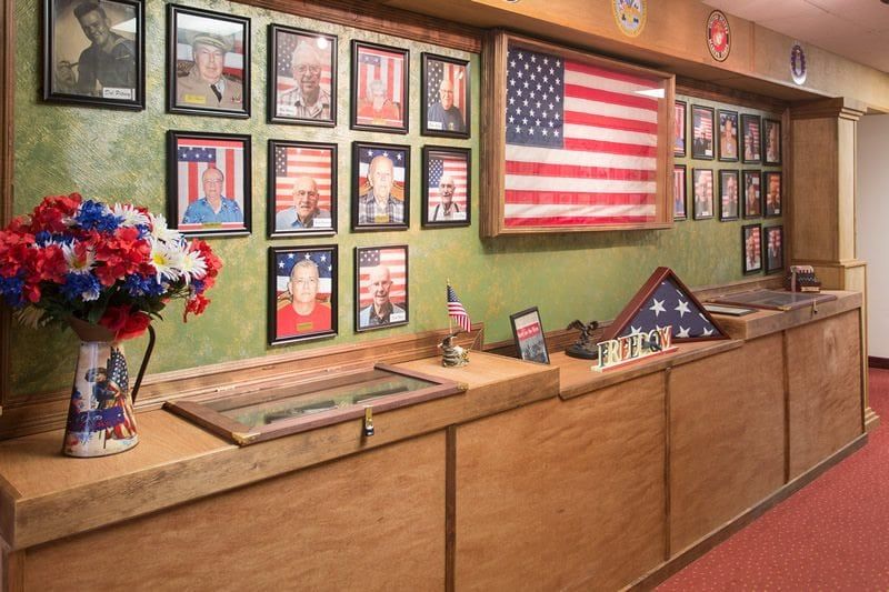 A wall displaying framed photographs and American flags, dedicated to honoring military service.