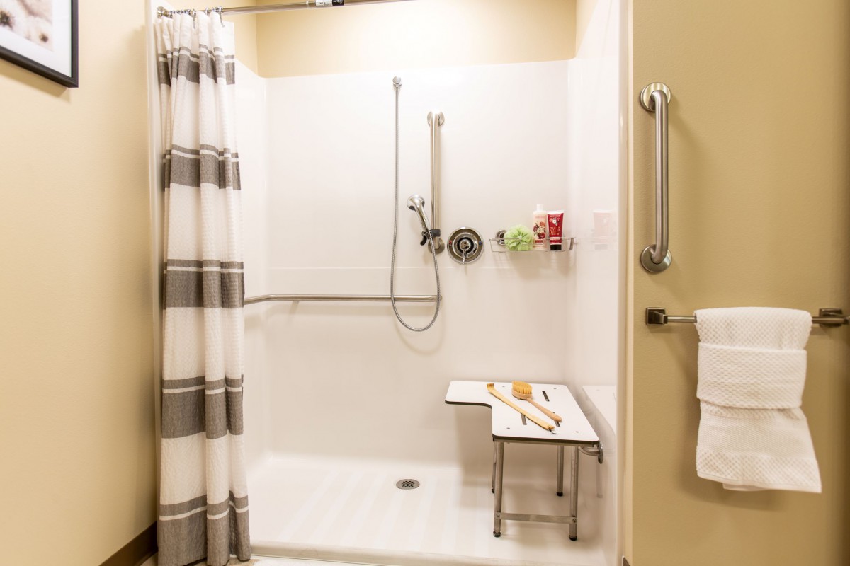 A modern, accessible bathroom shower equipped with a shower chair and grab bars.