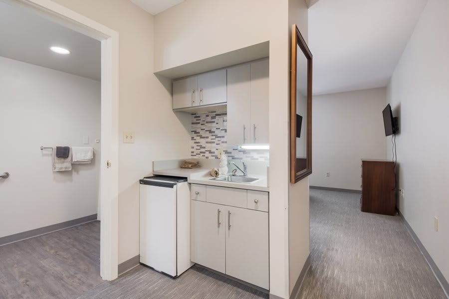 A compact kitchenette with a mini fridge, cabinet, sink, and microwave in an apartment.