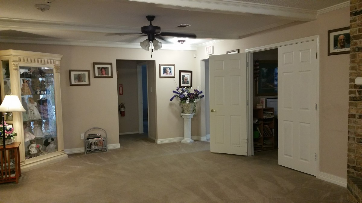 A spacious living room with a ceiling fan, decorated walls, and an open door leading to another room.