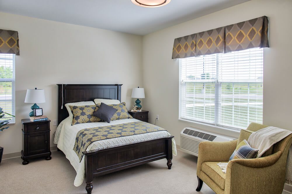 A cozy bedroom with a bed, armchair, and window providing natural light.