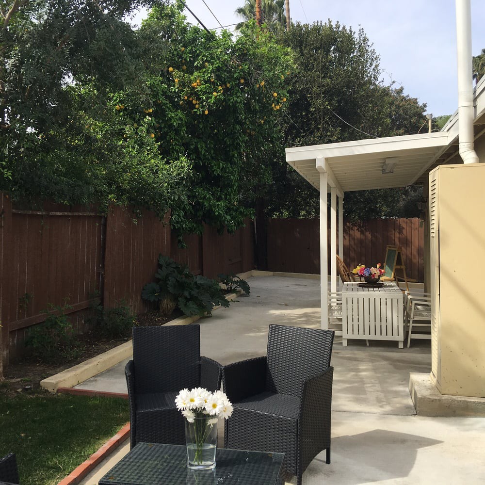 A cozy backyard patio with wicker furniture surrounded by lush greenery.