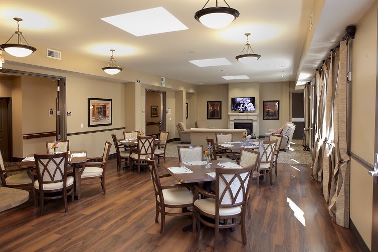 A well-lit dining area featuring multiple tables and chairs, adorned with wall art and wood flooring.