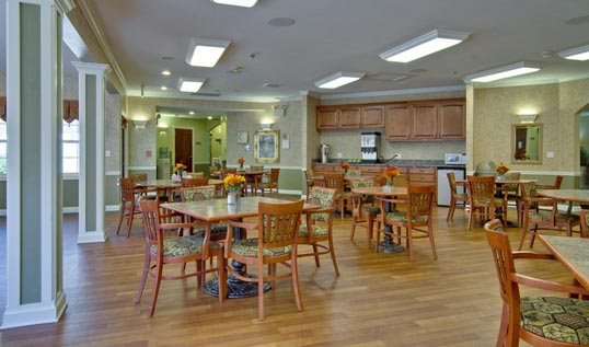 A spacious dining area with wooden tables and chairs, adjacent to a kitchen.