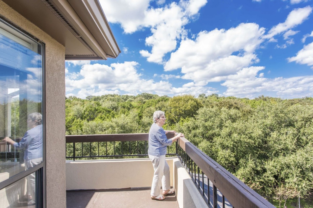 A person enjoying the view from a balcony overlooking a lush green landscape under a partly cloudy sky.
