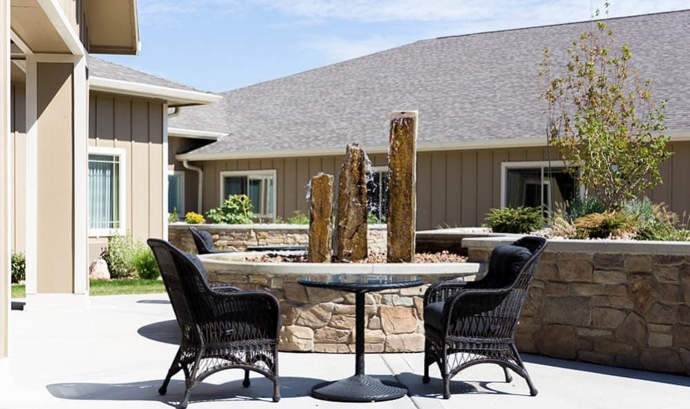 An outdoor patio area featuring a round table with wicker chairs and a decorative fountain centerpiece.