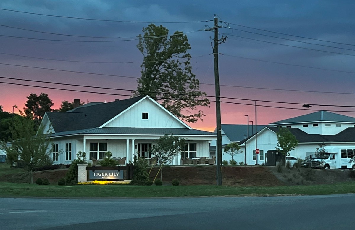 A charming house at sunset with a vibrant sky and surrounding trees.