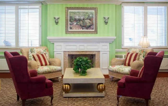 A cozy living room with green walls, featuring a white fireplace, comfortable armchairs, and a central coffee table adorned with a plant.