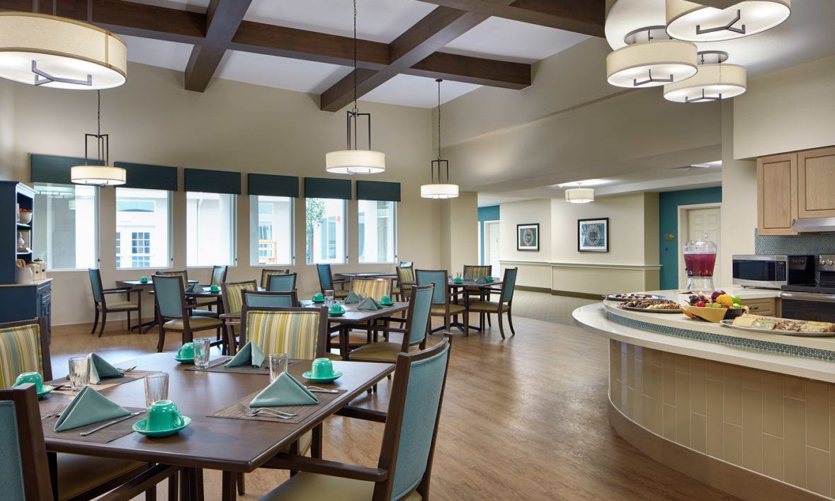 A well-lit dining room with neatly arranged tables and chairs, featuring elegant lighting and wooden flooring.