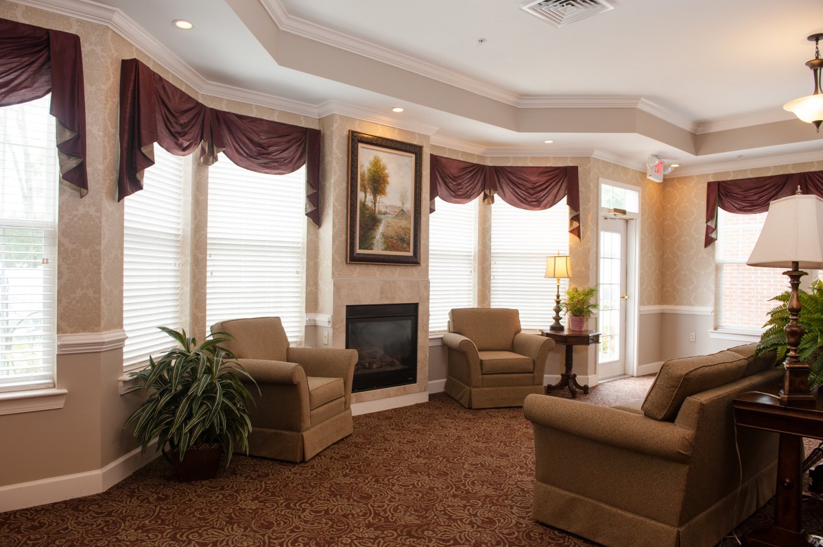 A cozy living room with armchairs arranged around a fireplace, featuring elegant window treatments and warm lighting.