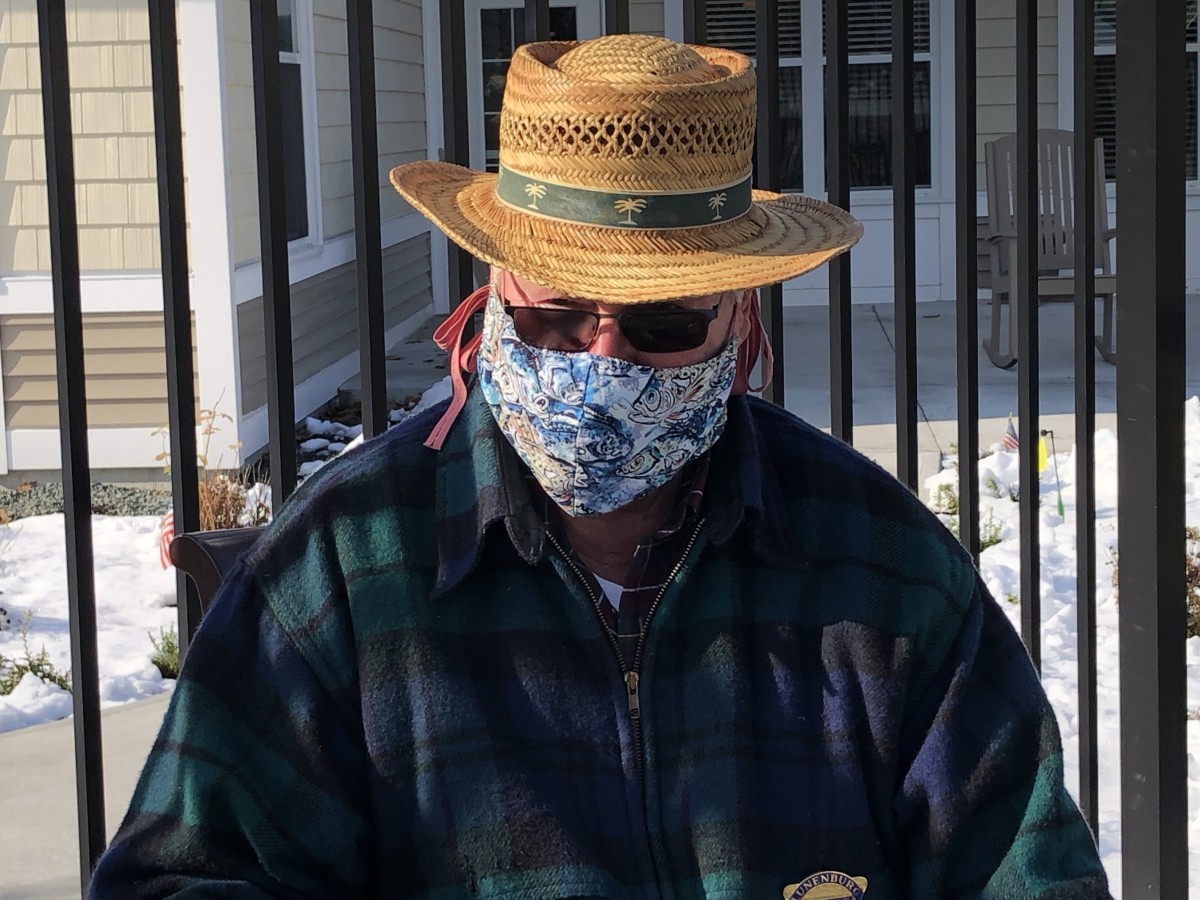 A person wearing a straw hat, sunglasses, and a floral face mask outdoors.