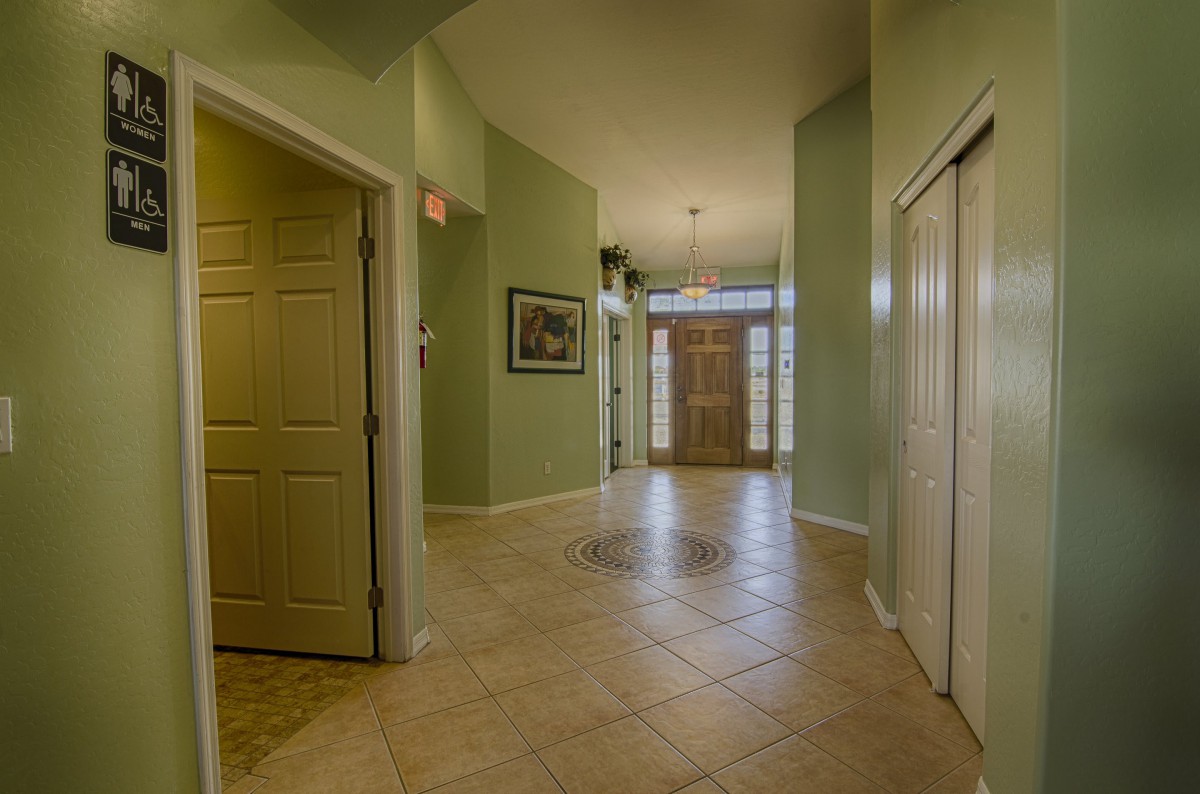A spacious hallway with green walls and a tiled floor leading to a wooden front door.