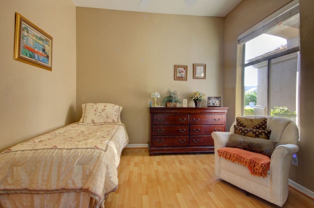 A cozy bedroom with a single bed, a wooden dresser, and a comfortable chair by the window.
